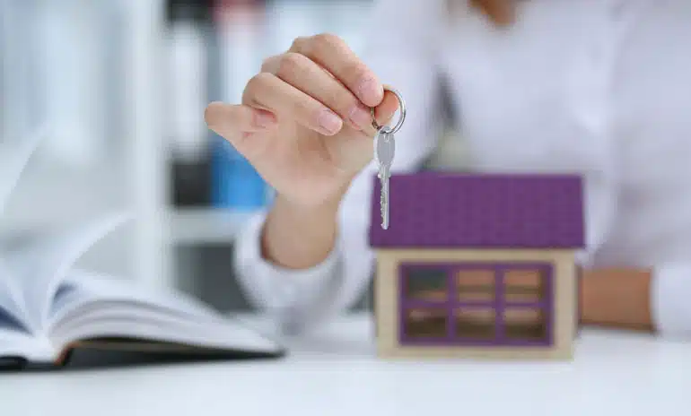 hand holding keys with a house replica on the table