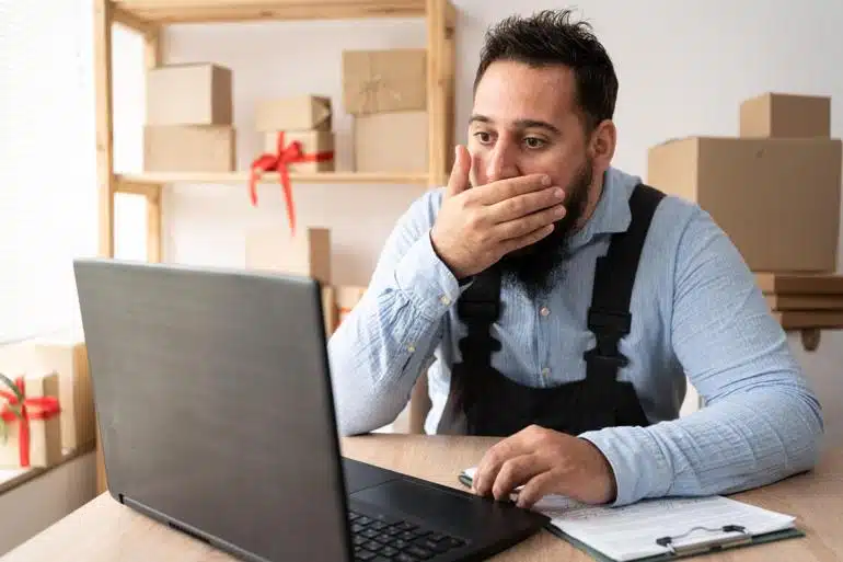 Online seller covering his mouth in fear while looking at his laptop