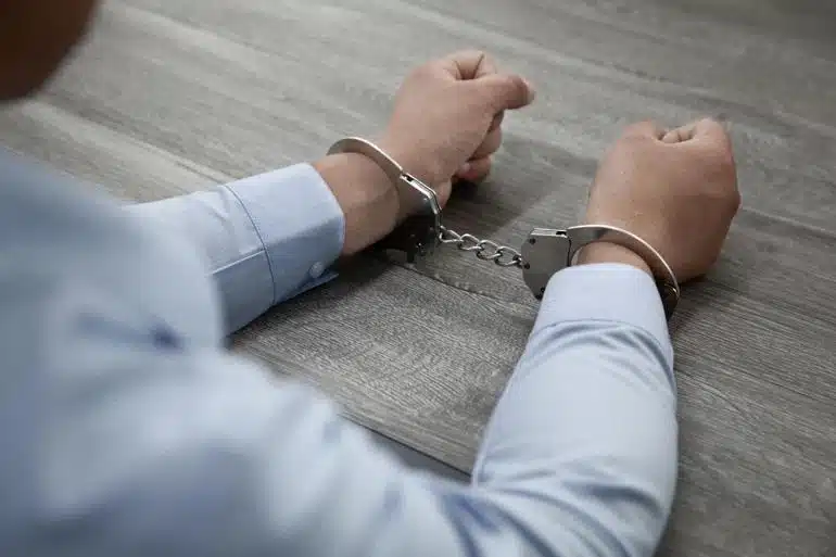 Closeup of a man wearing a dress shirt in handcuffs on a table.