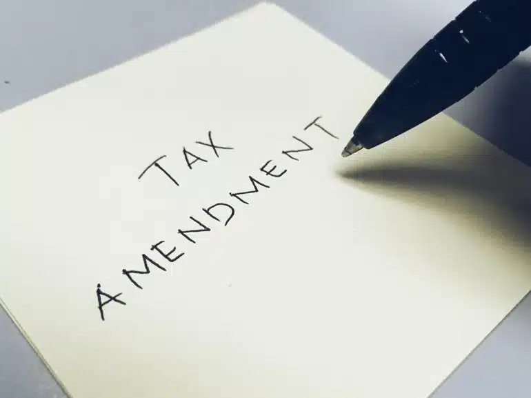 The words "Tax Amendment" written on a piece of paper with a pen hovering over it