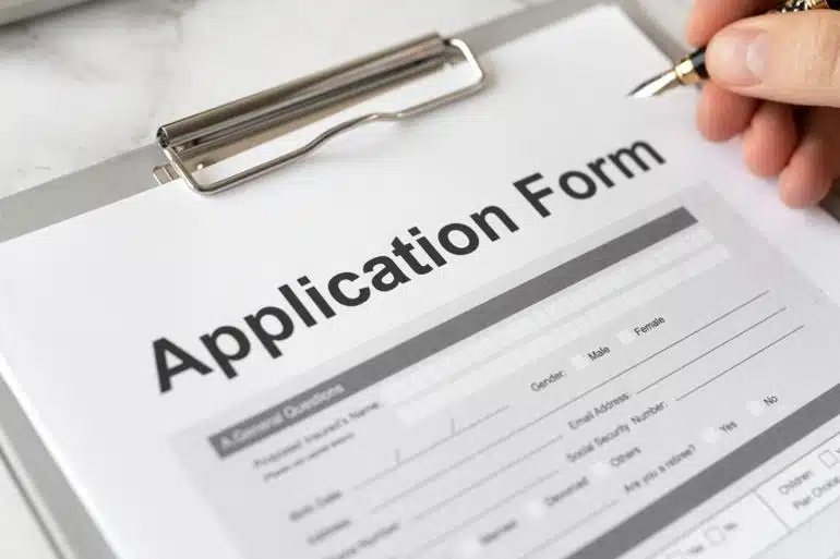 Close-up of a hand completing an application form on a clipboard using a pen.
