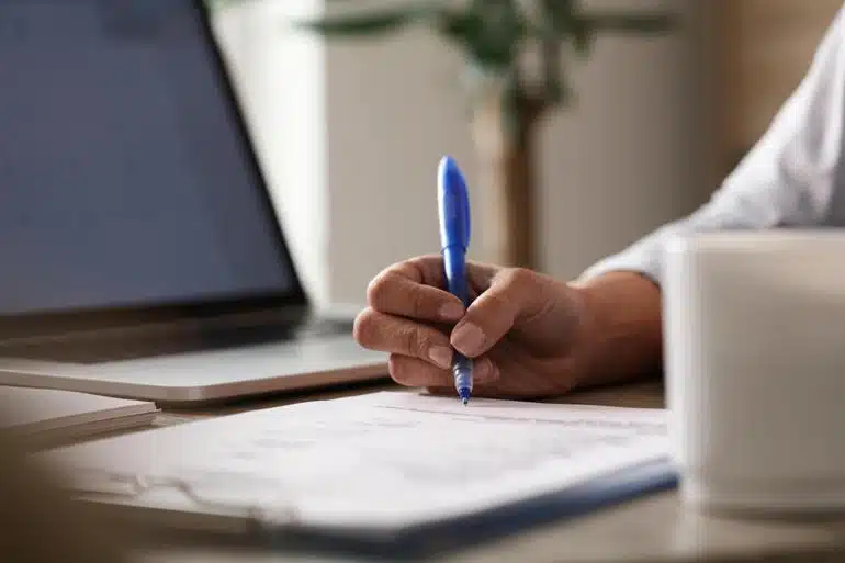 Close-up of a person signing a paper at a desk in an office.